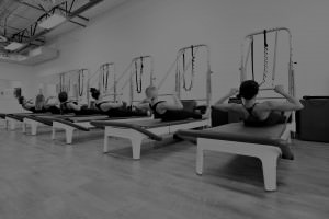 A row of people are practicing pilates on their reformer.